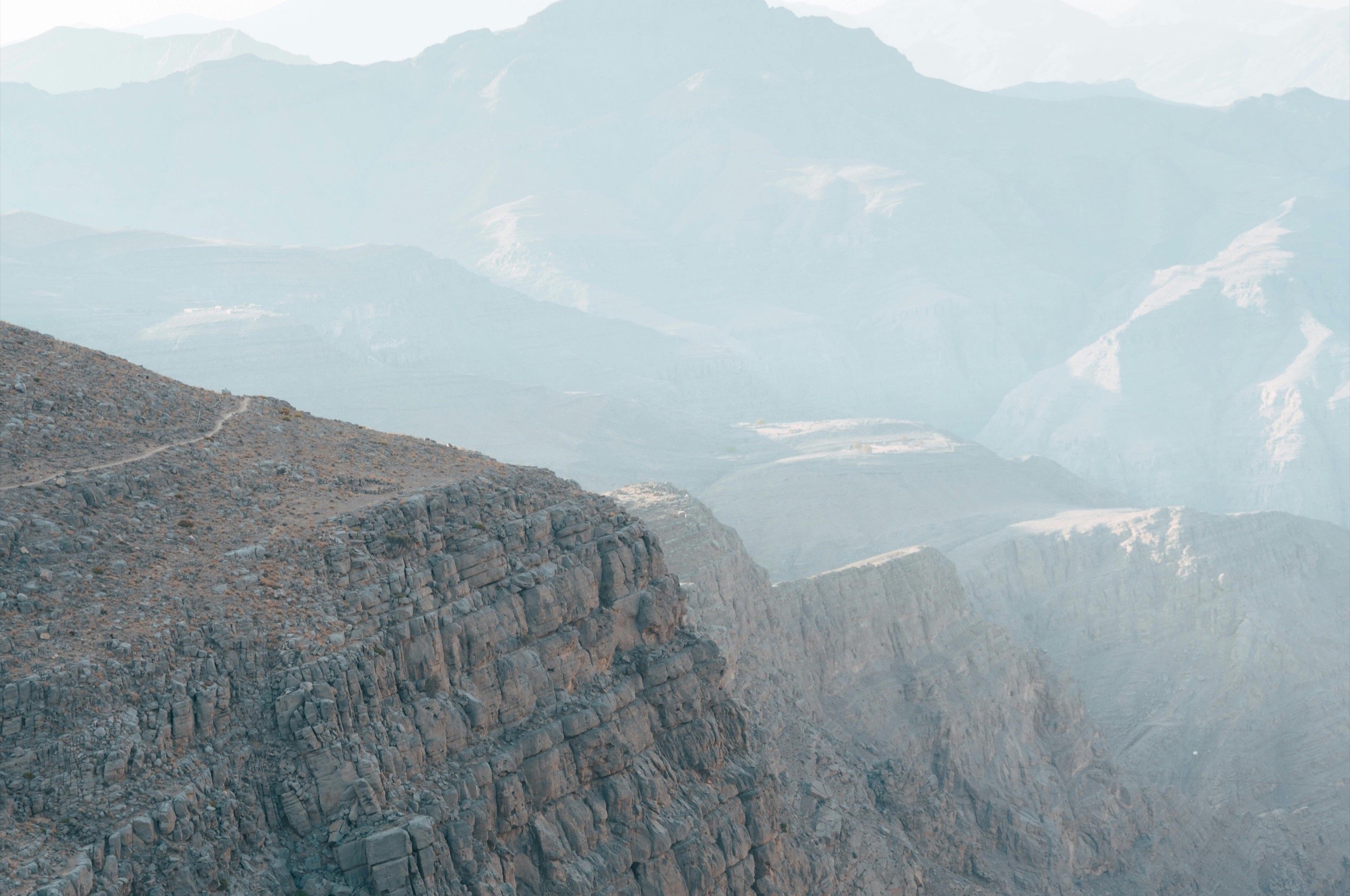 The rim of the Jebel Shams gorge, with the peaks of the Hajar Mountains in the morning haze