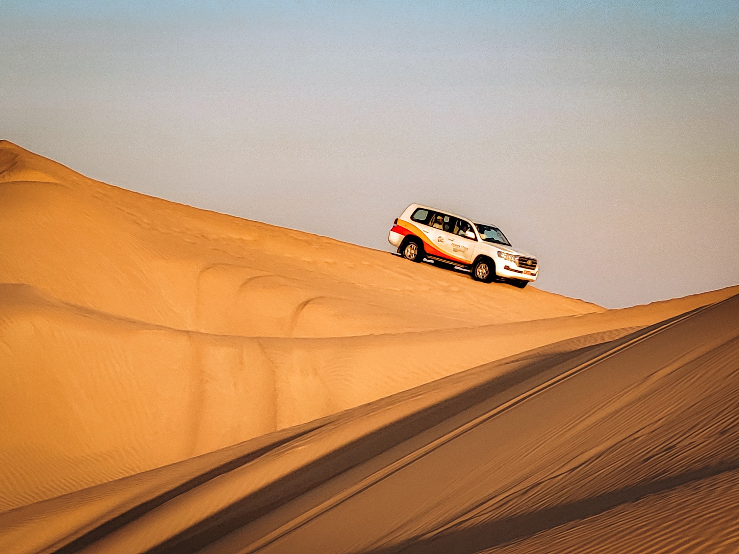 Driving a 4x4 across the Wahiba Sands dunes at golden hour